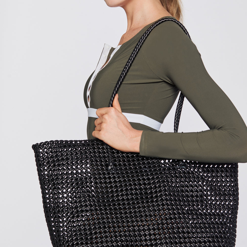 
                  
                    Woman holding a plastic woven black beach bag against a plain background.
                  
                