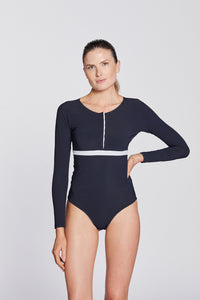 Front view of a woman wearing a marine blue swimsuit with long sleeves, white button strip and white line under the bust, in front of a white background.
