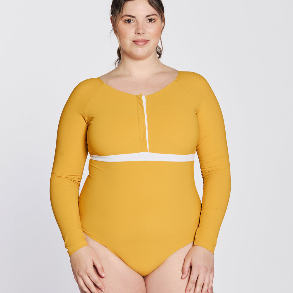 
                  
                    Front view of a woman wearing a sunflower yellow swimsuit with long sleeves, white button strip and white line under the bust, in front of a white background.
                  
                