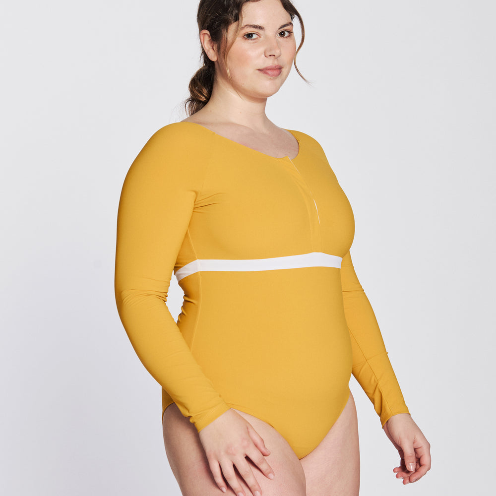 
                  
                    Side view of a woman wearing a sunflower yellow swimsuit with long sleeves, white button strip and white line under the bust, in front of a white background.
                  
                