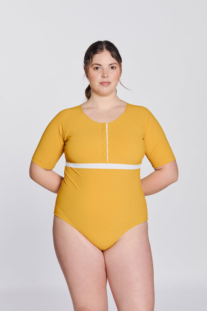 
                  
                    Front view of a woman wearing a sunflower yellow swimsuit with short sleeves, white button strip and white line under the bust, in front of a white background.
                  
                