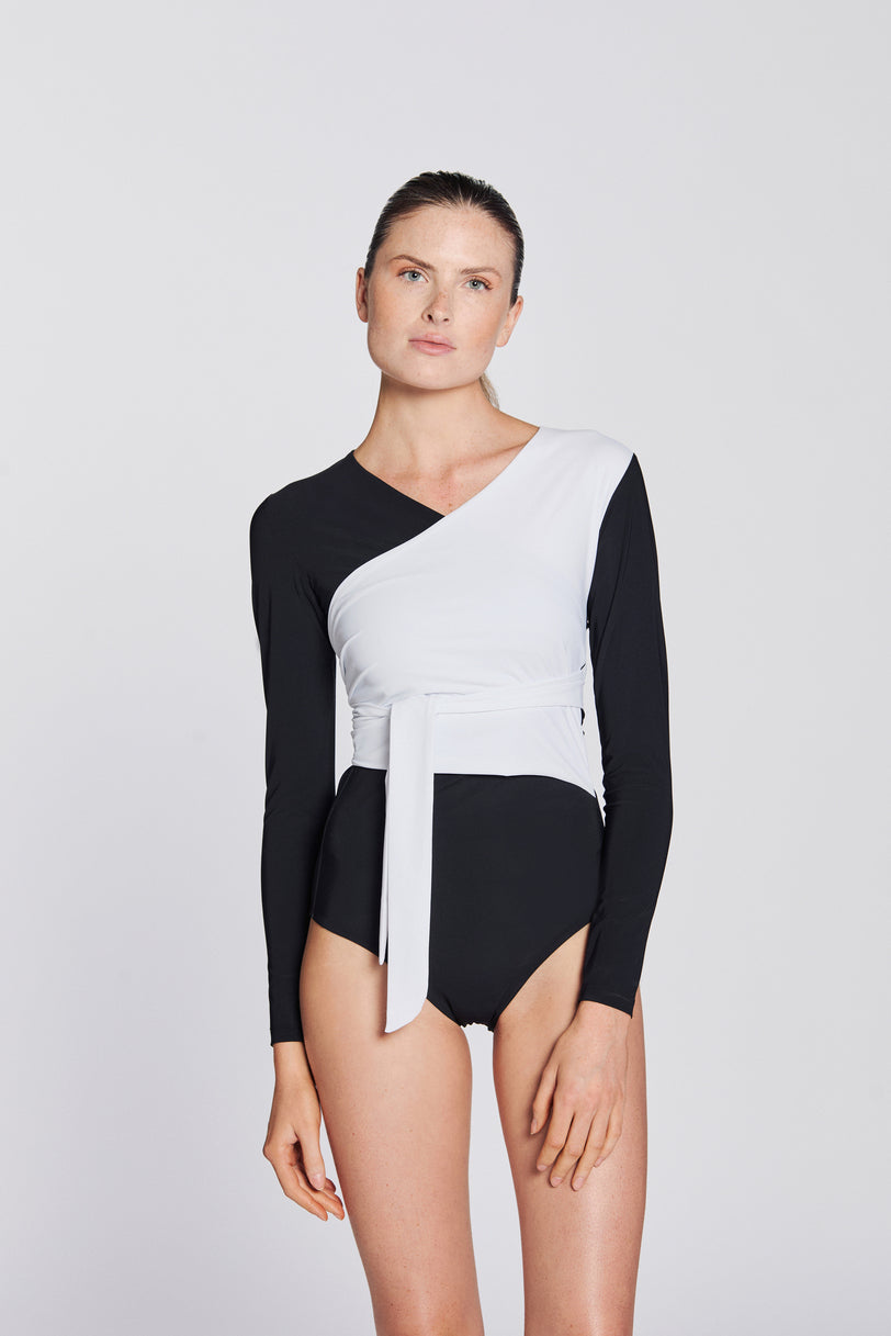Front view of a woman wearing a black and white asymmetrical swimsuit with long sleeves, on a white background.