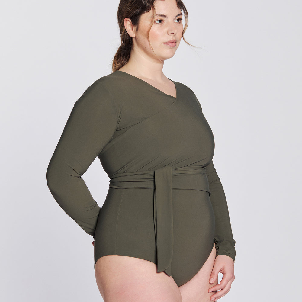 
                  
                    Side view of a woman wearing a hunter green swimsuit with long sleeves and wrap closing, in front of a white background.
                  
                