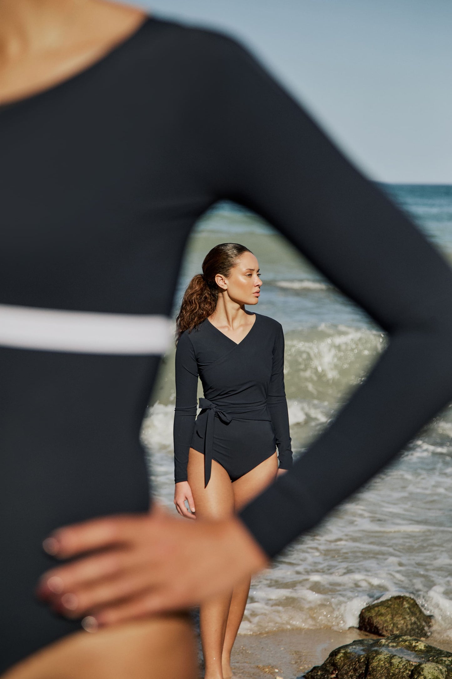 Woman wearing a marine blue swimsuit with long sleeves and wrap closing, in front of the sea.