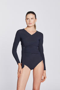 Front view of a woman wearing a marine blue swimsuit with long sleeves and wrap closing, in front of a white background.