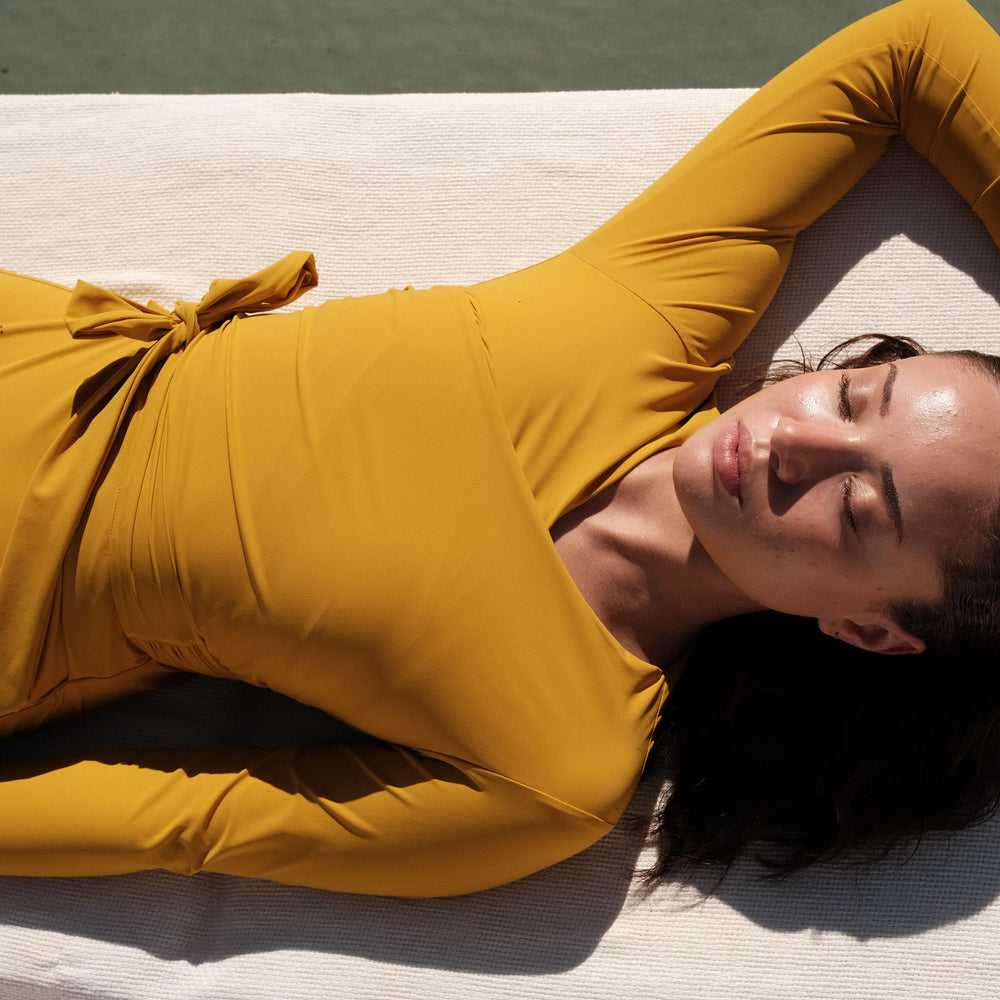 Woman wearing a sunflower yellow swimsuit with long sleeves and wrap closing, laying at a swimming pool.