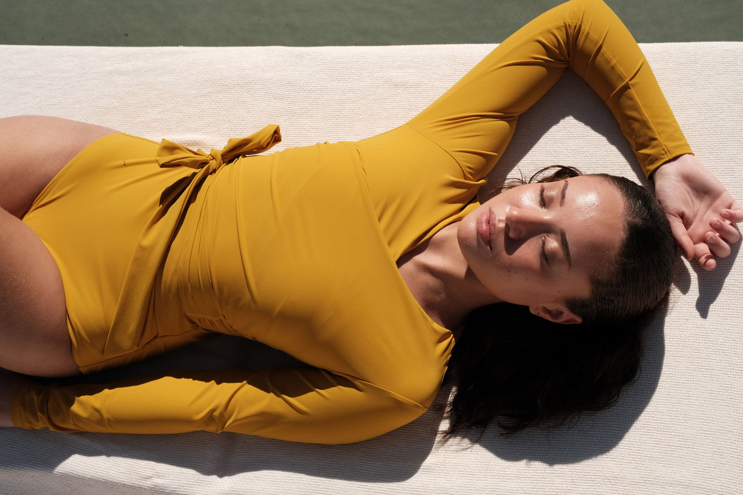 Woman wearing a sunflower yellow swimsuit with long sleeves and wrap closing, laying at a swimming pool.