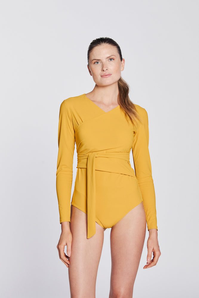 
                  
                    Front view of a woman wearing a sunflower yellow swimsuit with long sleeves and wrap closing, in front of a white background.
                  
                