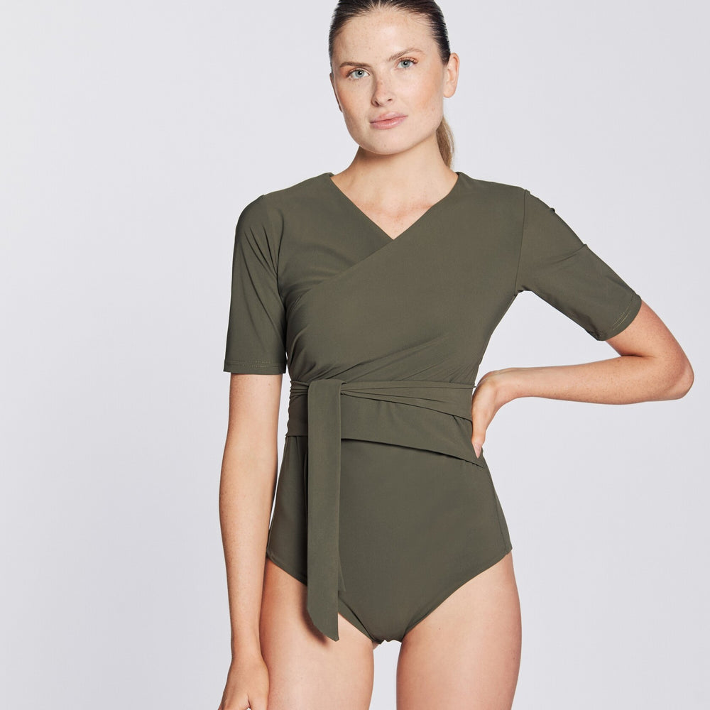 Front view of a woman wearing a hunter green swimsuit with short sleeves and wrap closing, in front of a white background.