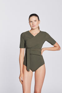 Front view of a woman wearing a hunter green swimsuit with short sleeves and wrap closing, in front of a white background.