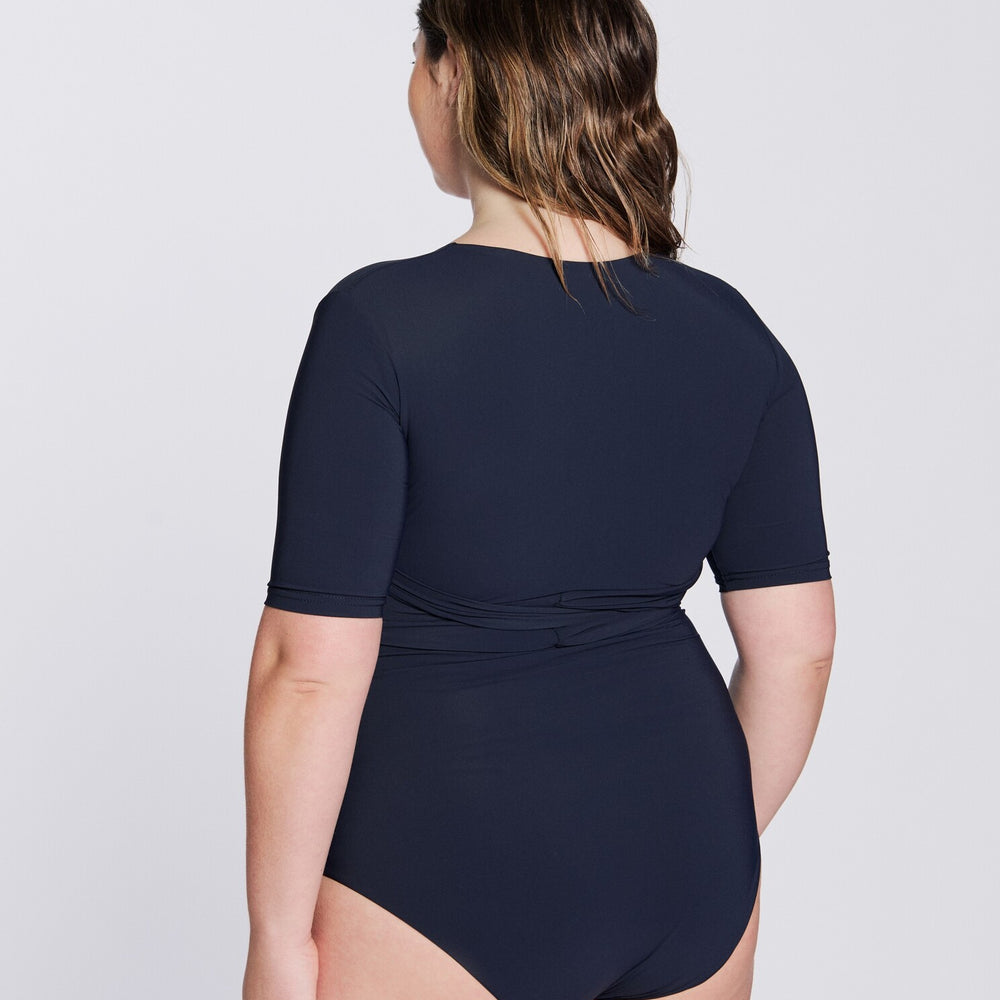 
                  
                    Back view of a woman wearing a marine blue swimsuit with short sleeves and wrap closing, in front of a white background.
                  
                