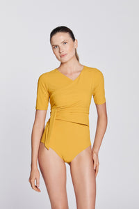 Front view of a woman wearing a sunflower yellow swimsuit with short sleeves and wrap closing, in front of a white background.