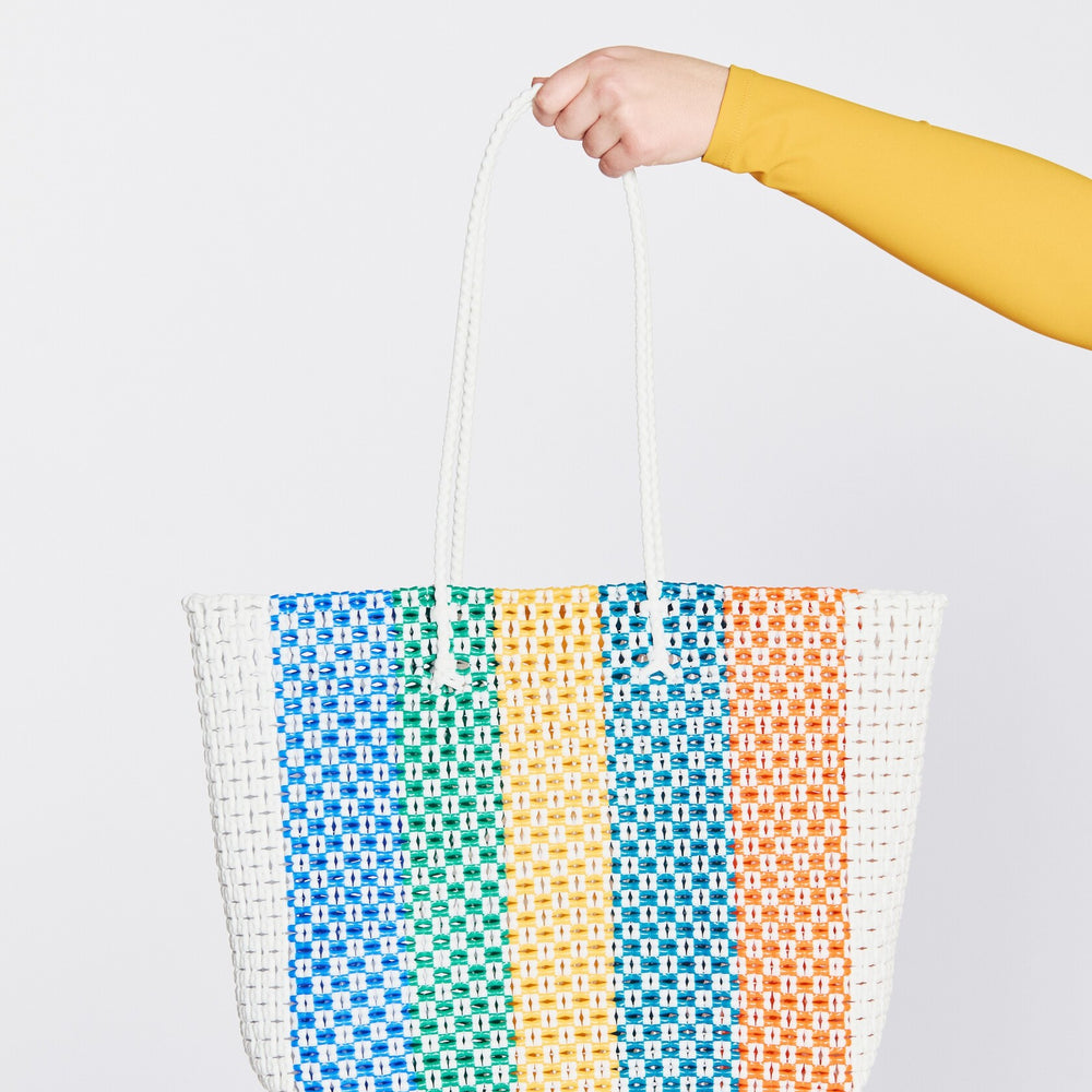
                  
                    Woven beach bag with colorful pattern held by a person against a white background.
                  
                