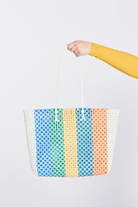 Woven beach bag with colorful pattern held by a person against a white background.
