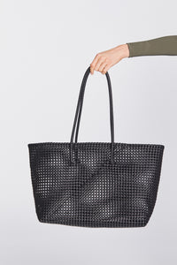 Plastic woven black beach bag held by a hand against a light gray background.